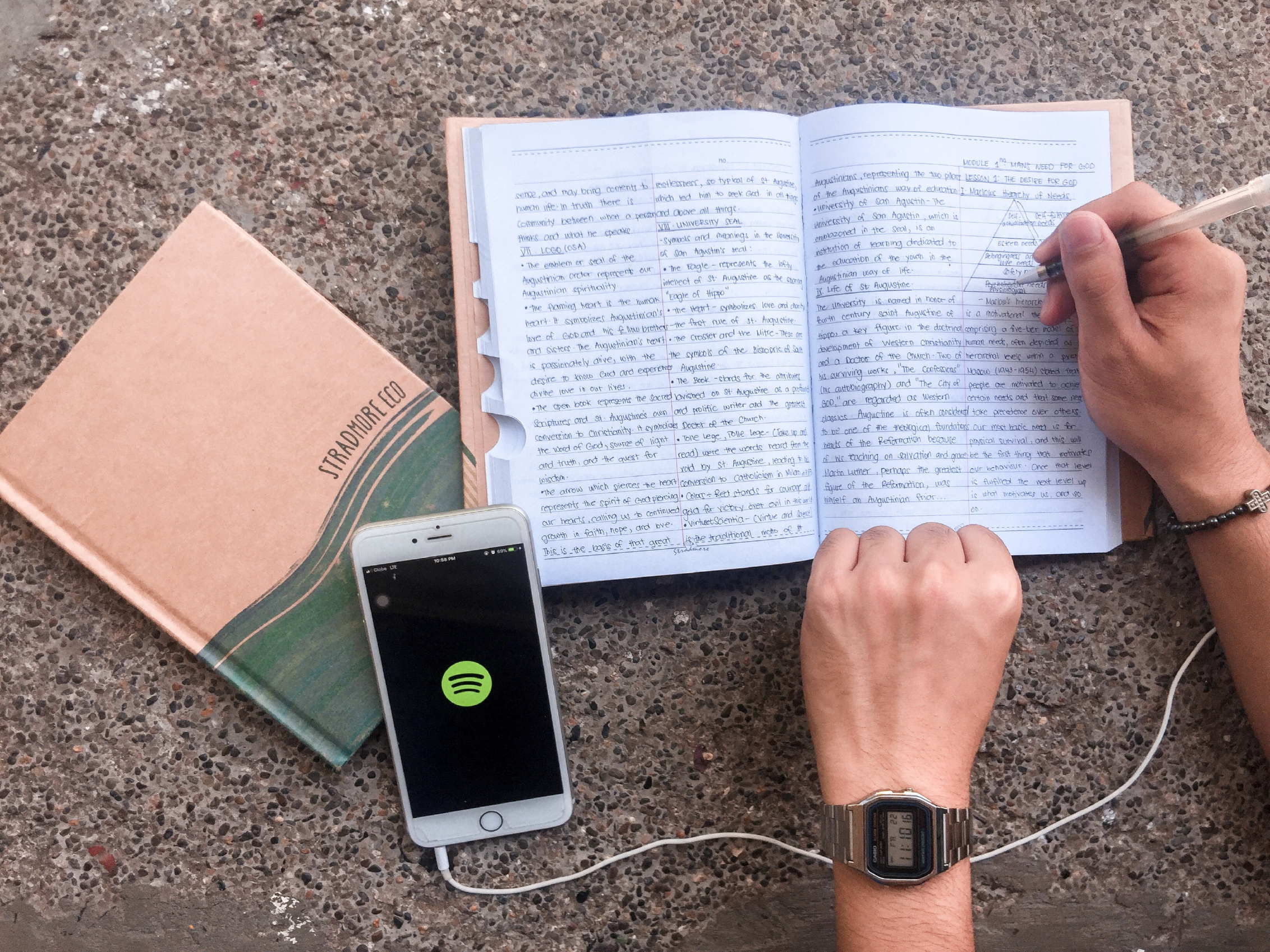 person writing on notebook & listening music